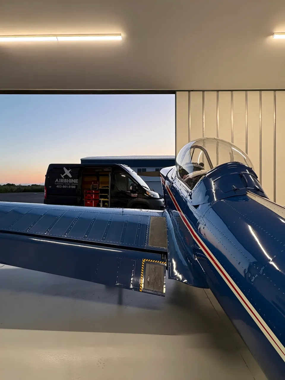 Deep-gloss fuselage in the hangar doorway at dusk